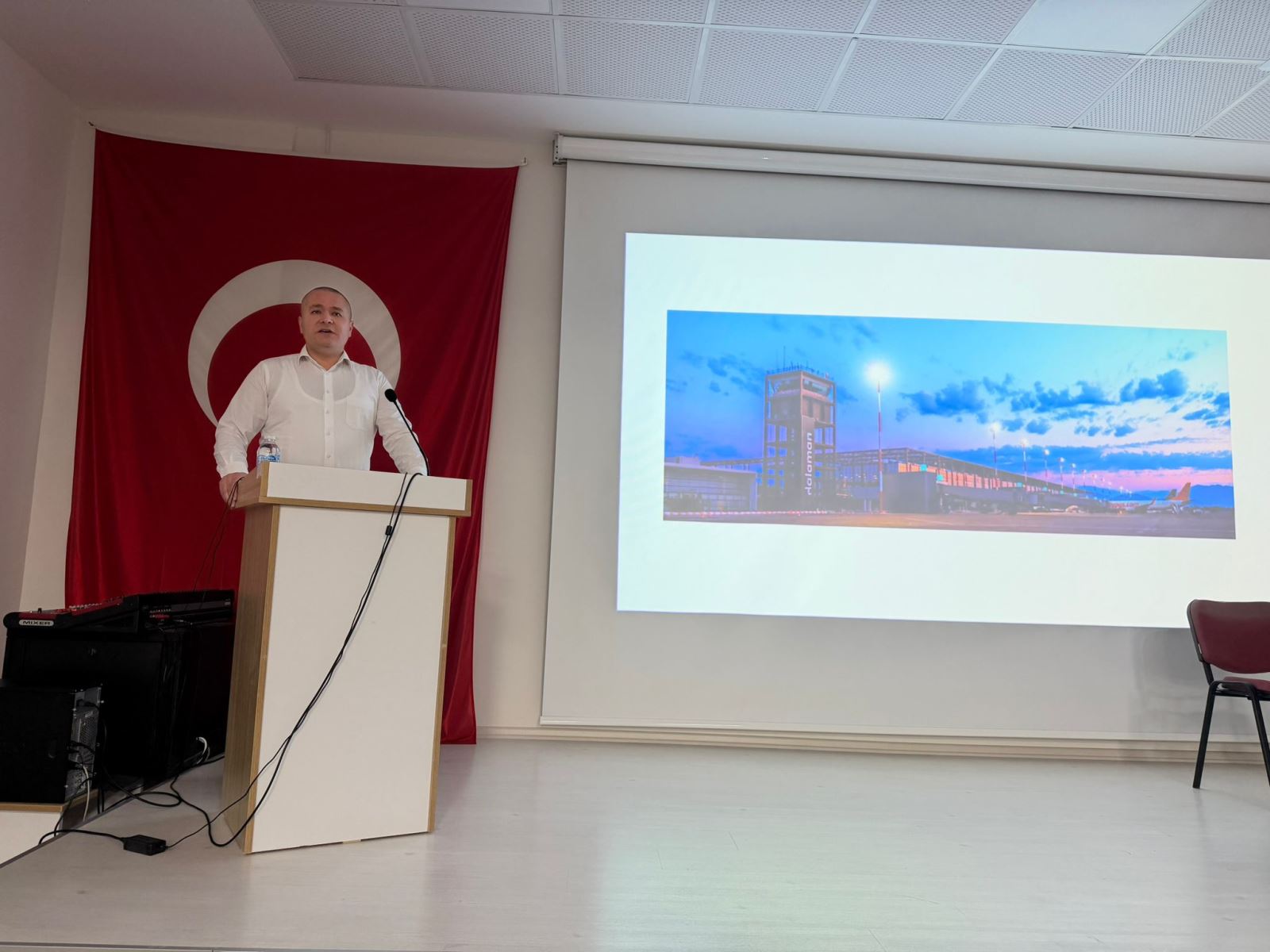 Kürsüde konuşma yapılan bu karede, arka plandaki dev Türk bayrağı ve projeksiyon ekranındaki Dalaman Havalimanı kulesi görseli dikkat çekiyor. Ciddi bir hitabet anını yansıtan bu fotoğraf, etkinliğin kurumsal ve resmi havasını başarıyla ön plana çıkarıyor.